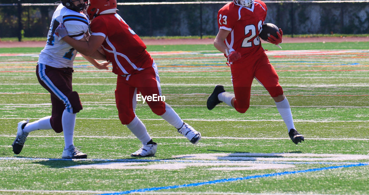 sports, player, competition, ball game, american football, athlete, team sport, soccer, clothing, group of people, sports uniform, motion, football player, activity, stadium, full length, adult, headwear, sport venue, sports equipment, grass, helmet, cooperation, running, men, sports team, football helmet, competitive sport, sports helmet, young adult, person, teamwork, tackle, american football - ball, sports clothing, tournament