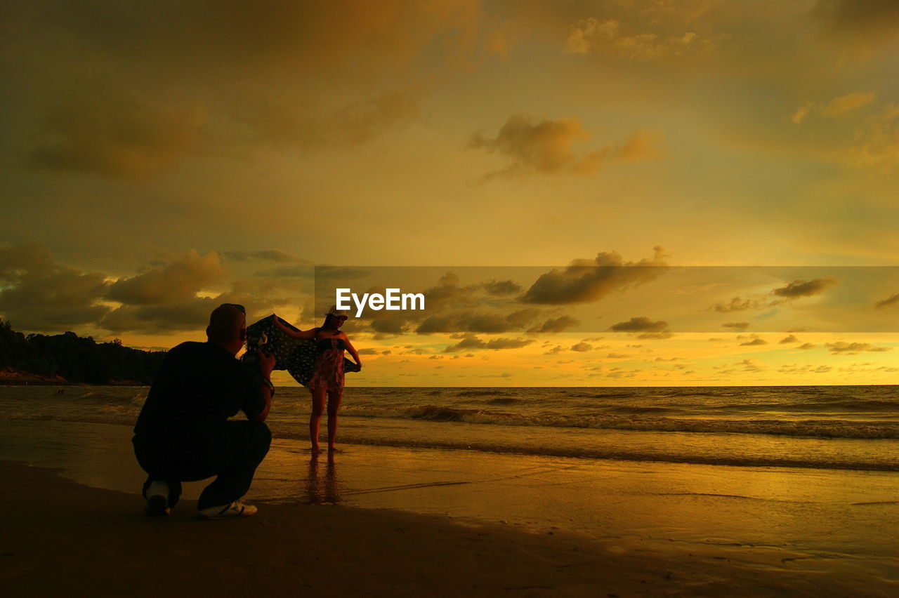 REAR VIEW OF SILHOUETTE FRIENDS STANDING ON BEACH AGAINST SKY