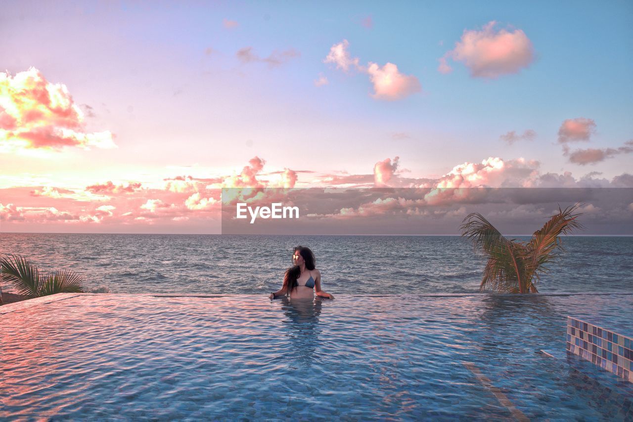 People sitting on infinite pool against sky during cuban sunset