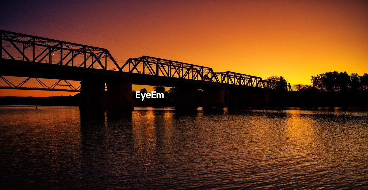 BRIDGE OVER RIVER AGAINST ORANGE SKY