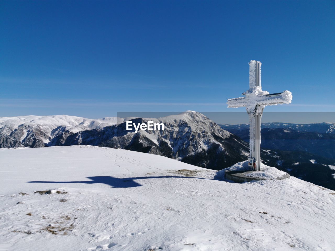 Cross on snowcapped mountain against blue sky