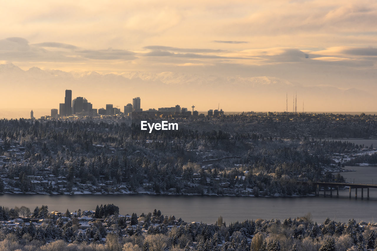CITYSCAPE BY RIVER AGAINST SKY DURING SUNSET