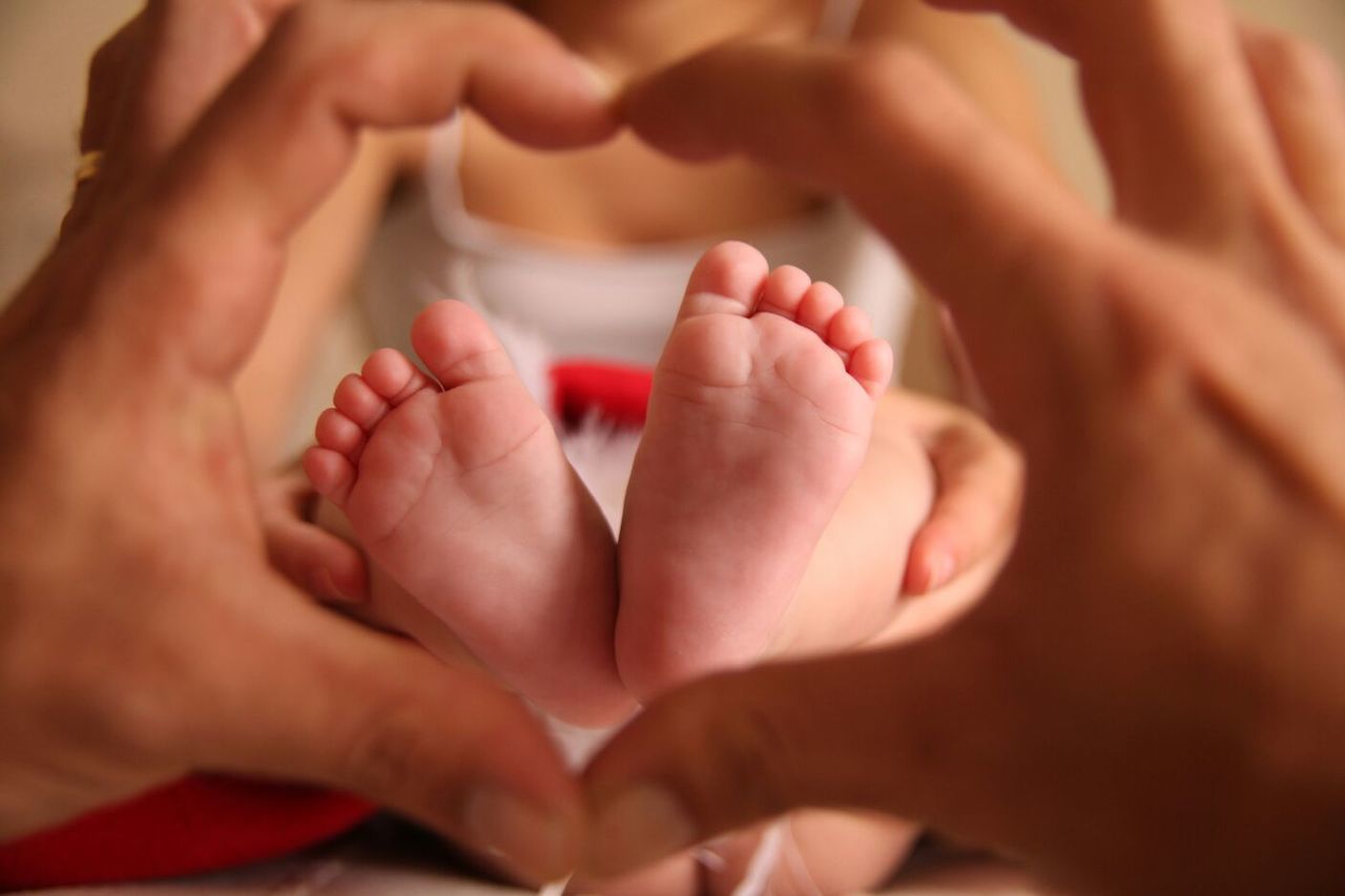 Hands forming heart shape against baby feet