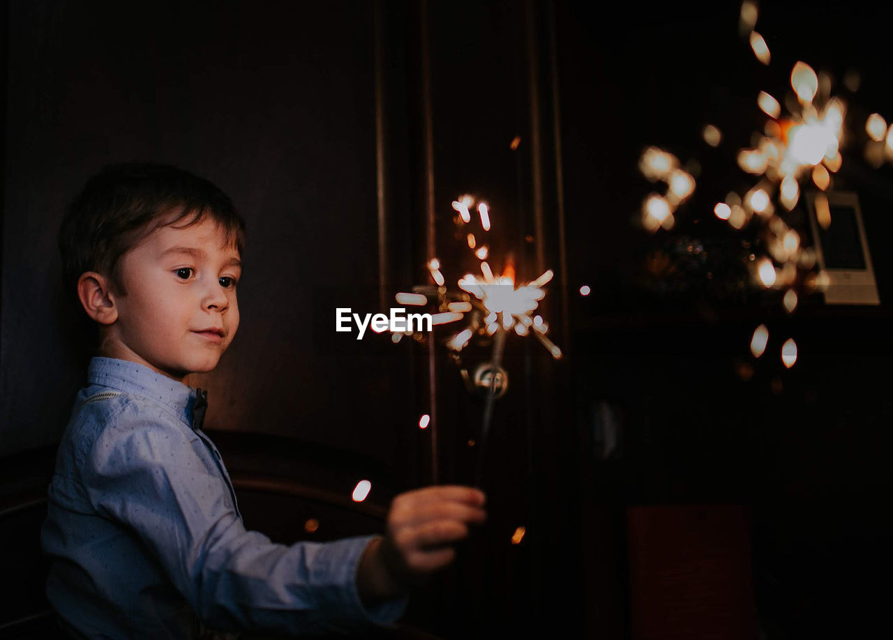 Boy looking while holding sparkler at night