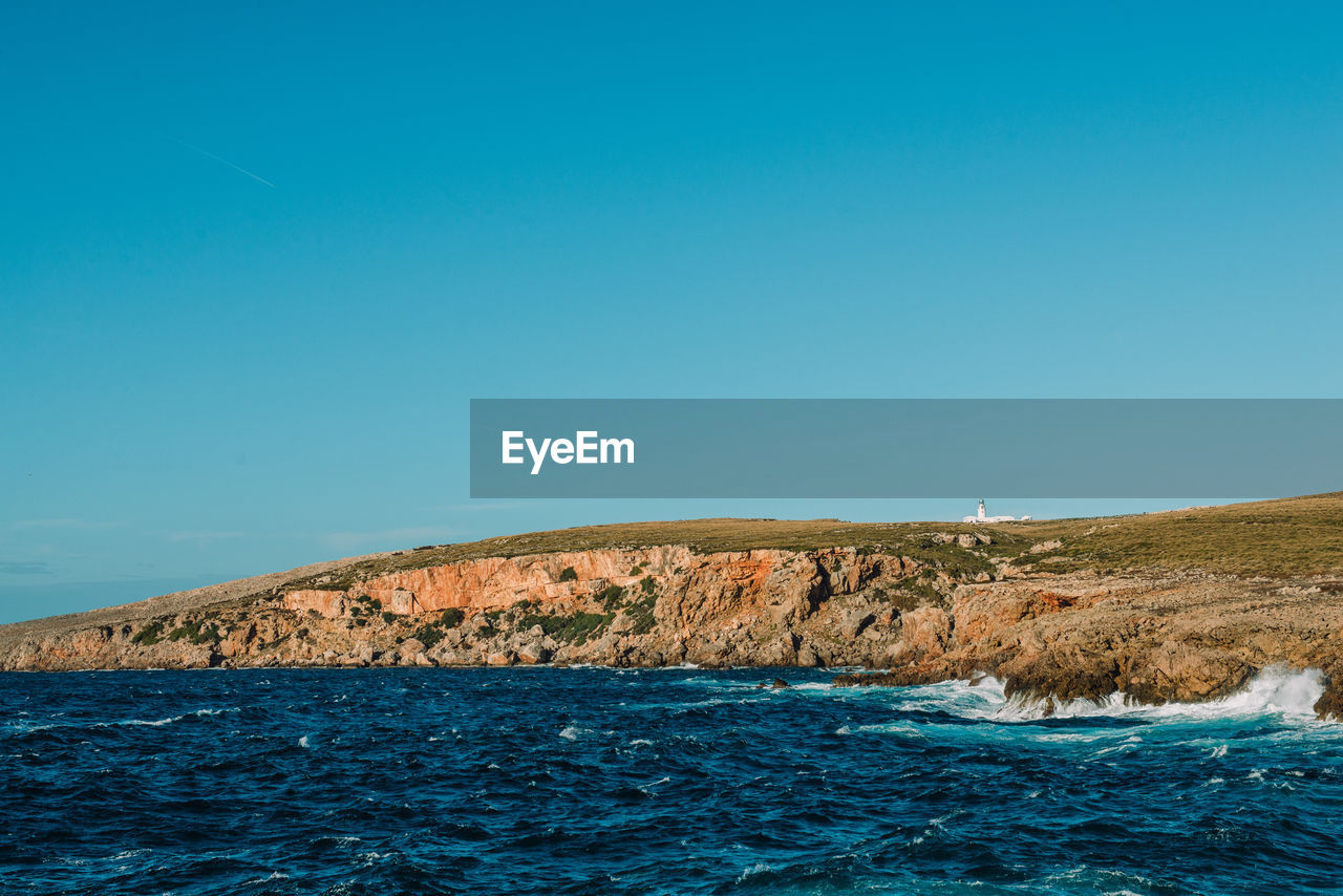 Scenic view of sea and cliff against clear blue sky