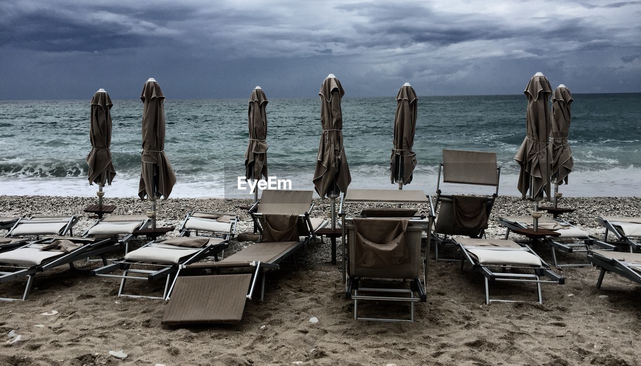 LOUNGE CHAIRS ON BEACH AGAINST SKY