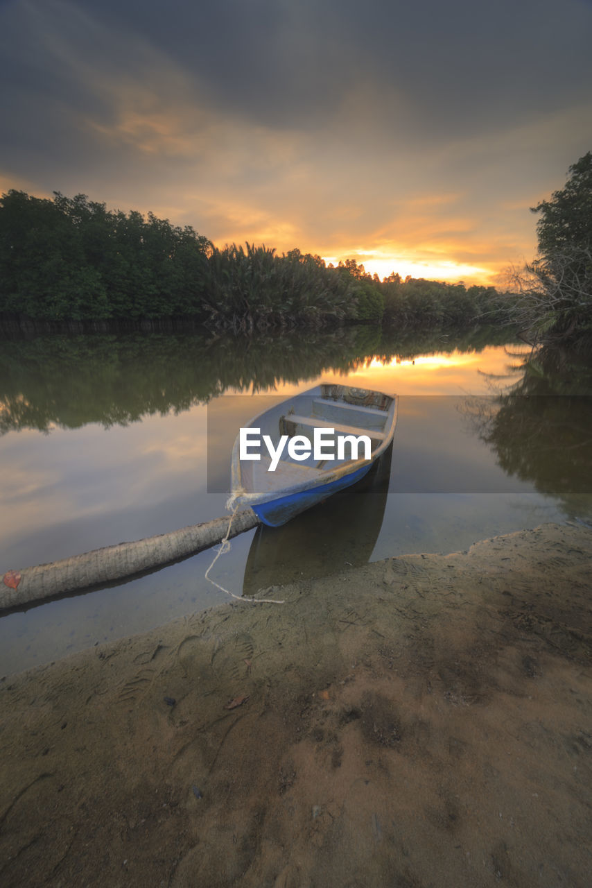 BOAT MOORED ON SHORE AGAINST SKY AT SUNSET