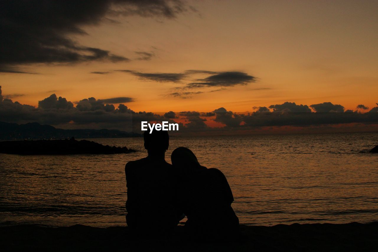 Silhouette couple sitting against orange sky during sunset