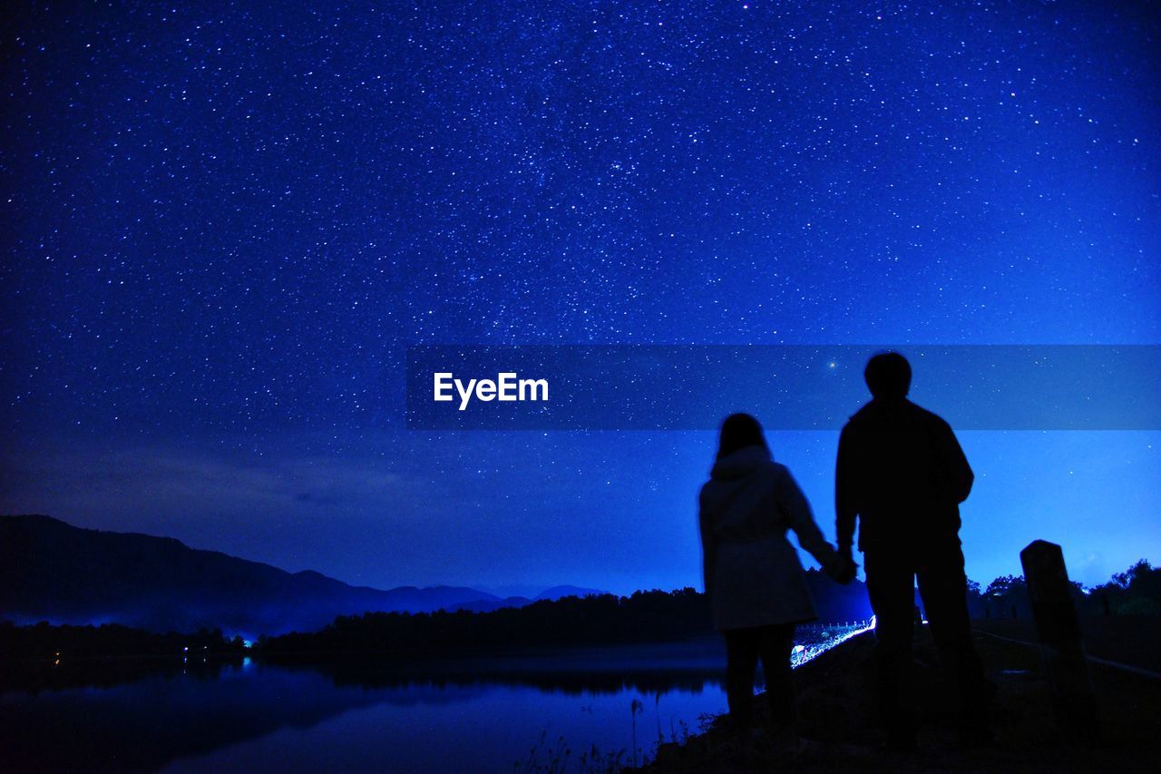 Silhouette couple standing against star field in sky at night