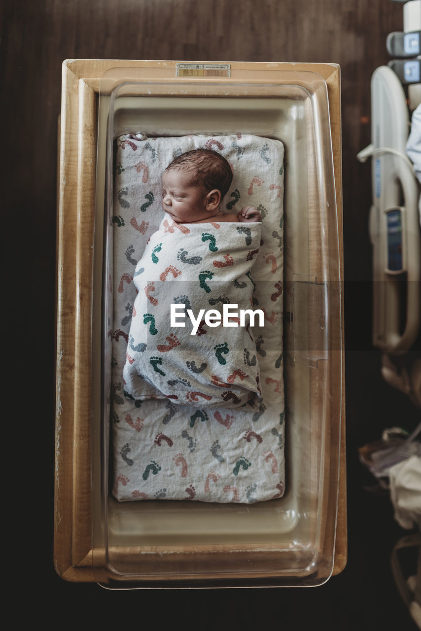 Overhead view of newborn baby boy in hospital bassinet with blankets