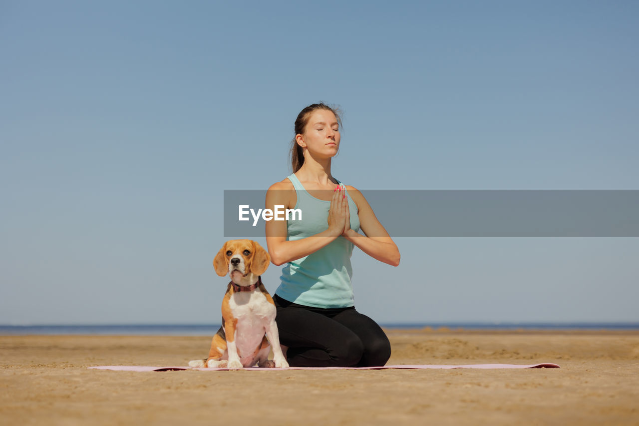 portrait of young woman holding dog at beach against clear sky