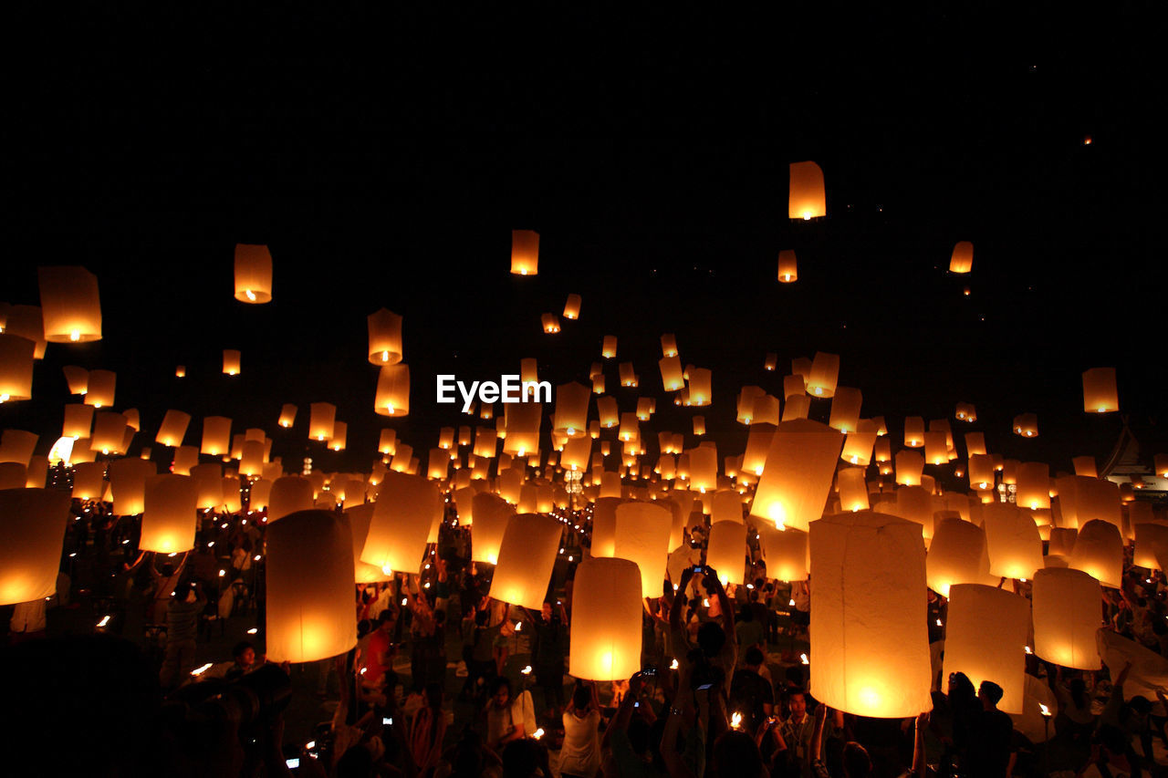 People with illuminated lanterns against sky at night
