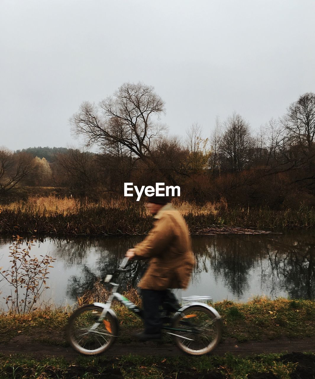 Side view of man riding bicycle by lake against sky