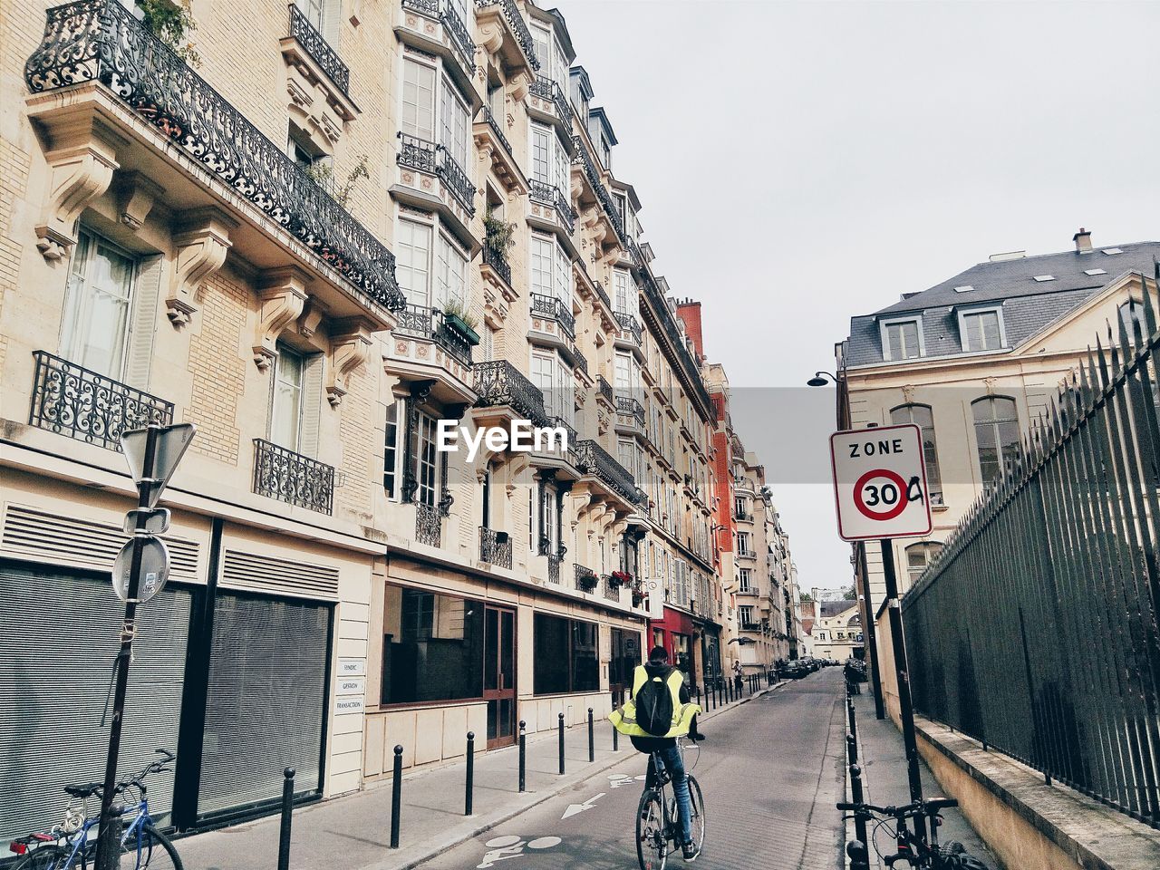 Rear view of man riding bicycle on street amidst building