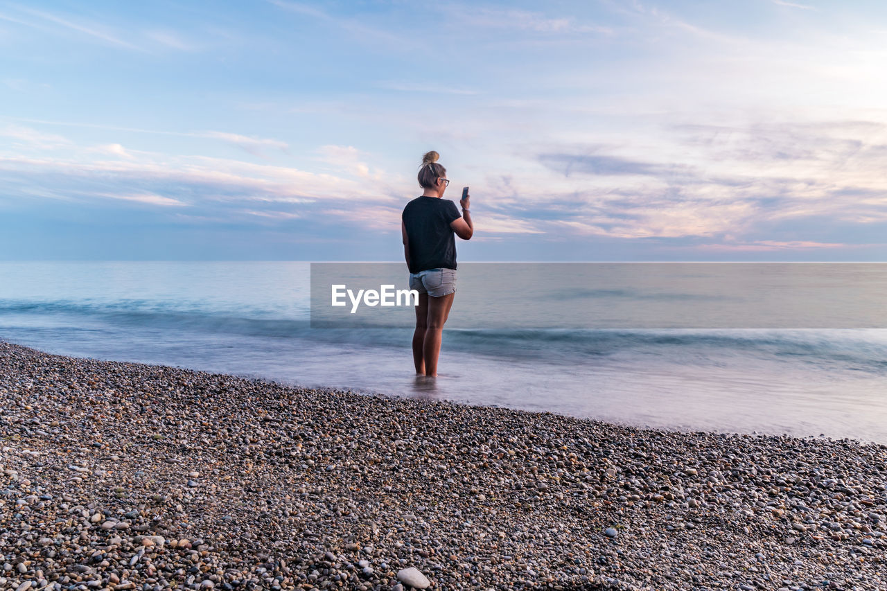 Woman standing on beach against sunset sky