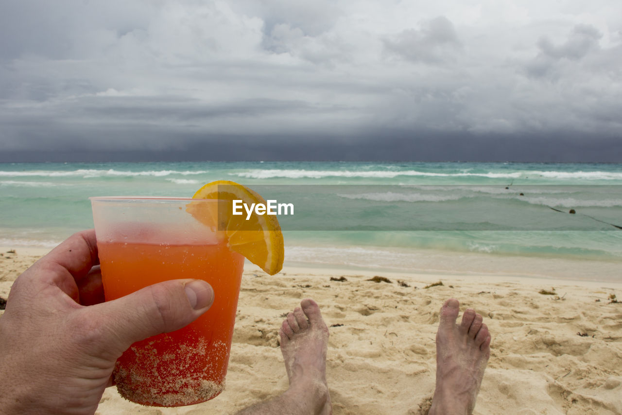 CLOSE-UP OF HAND HOLDING DRINK AT BEACH