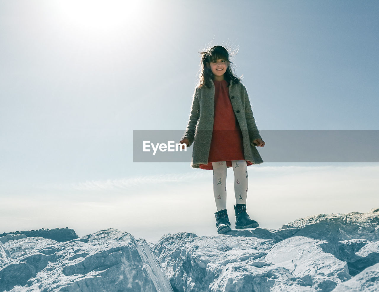Full length of girl standing on rocks against sky during winter