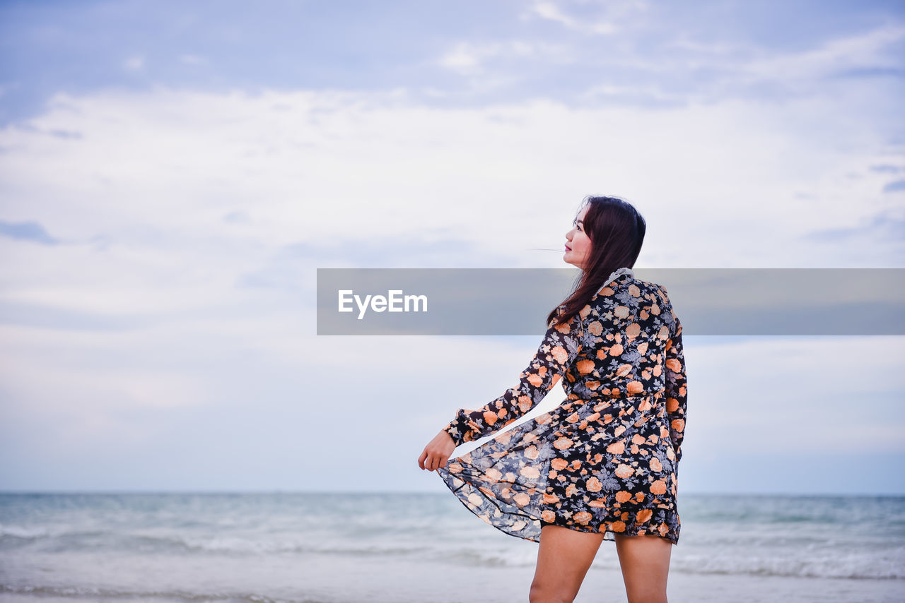 Woman wearing dress standing at beach against sky