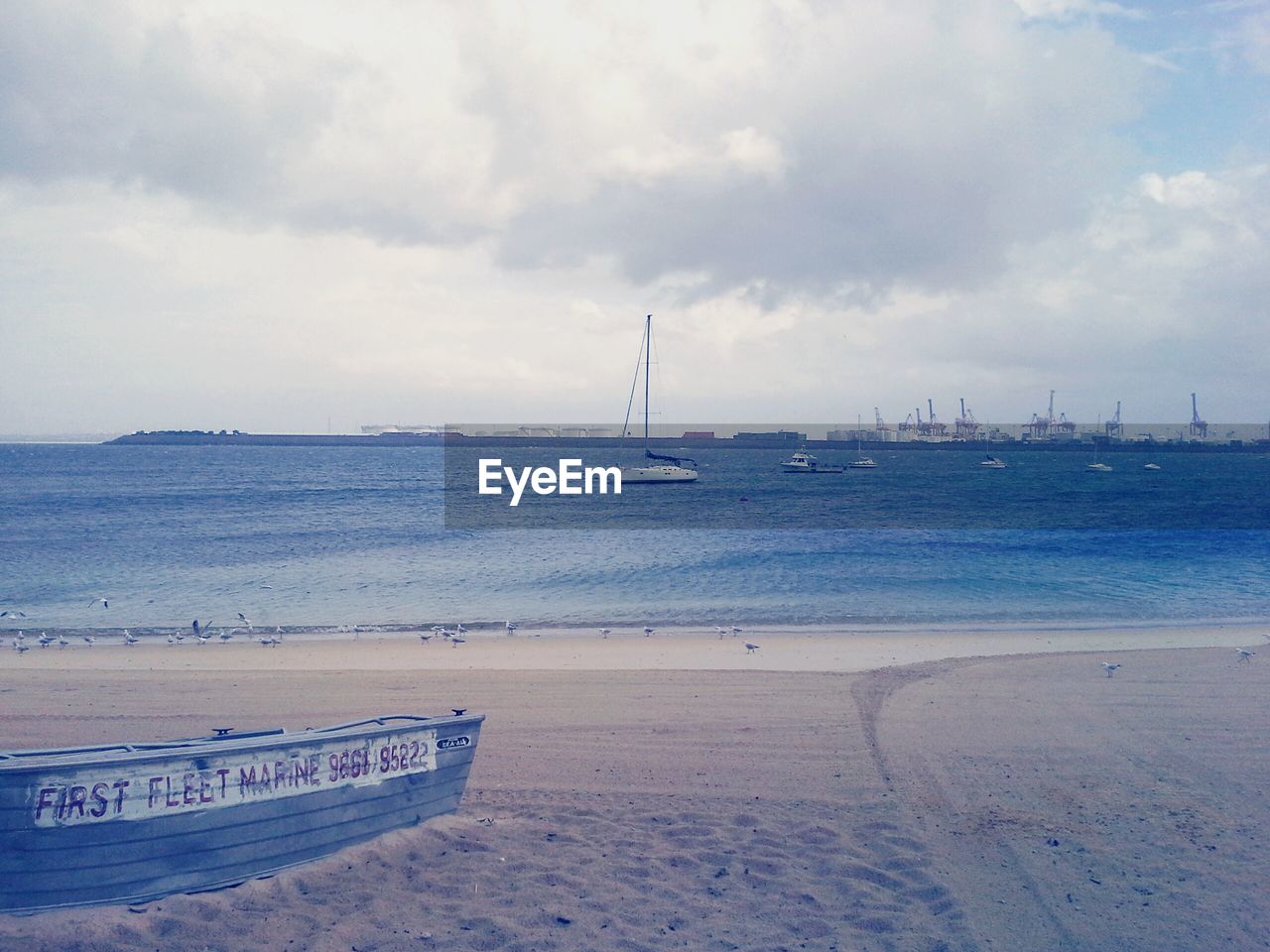 BOATS ON BEACH AGAINST CLOUDY SKY