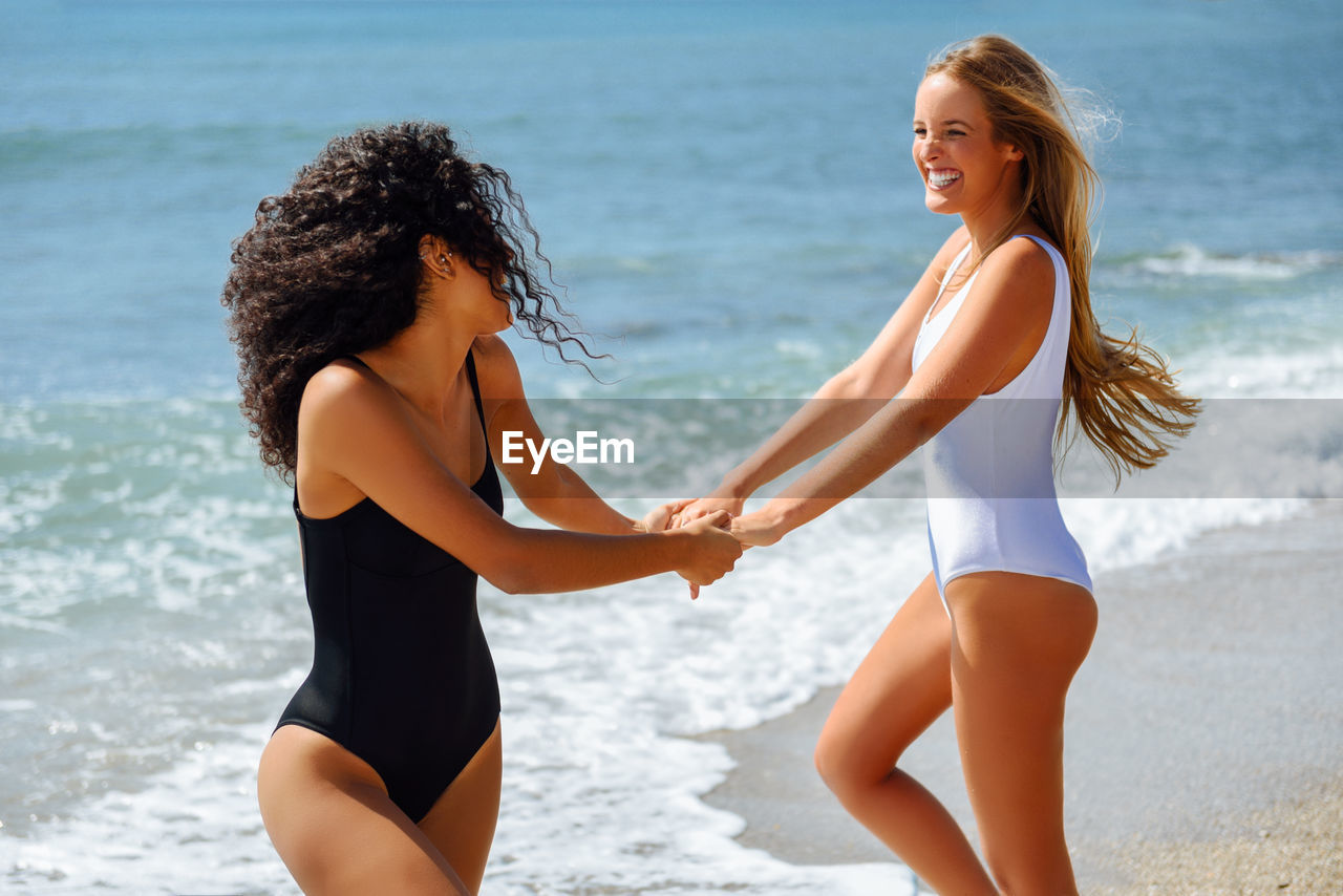 Sensuous female friends holding hands on shore at beach