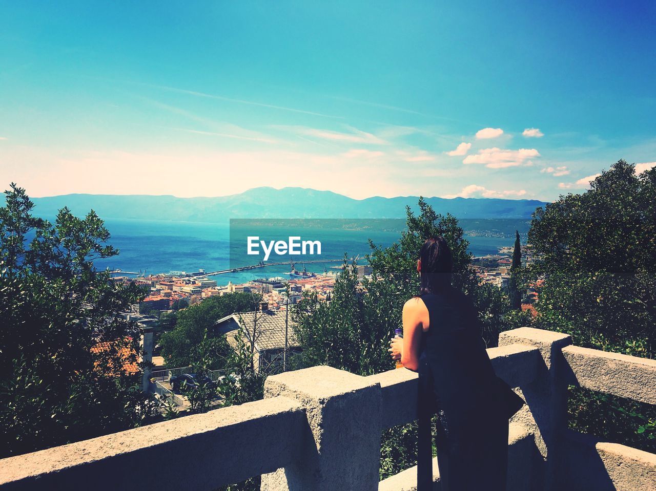 Rear view of woman at terrace against sky on sunny day