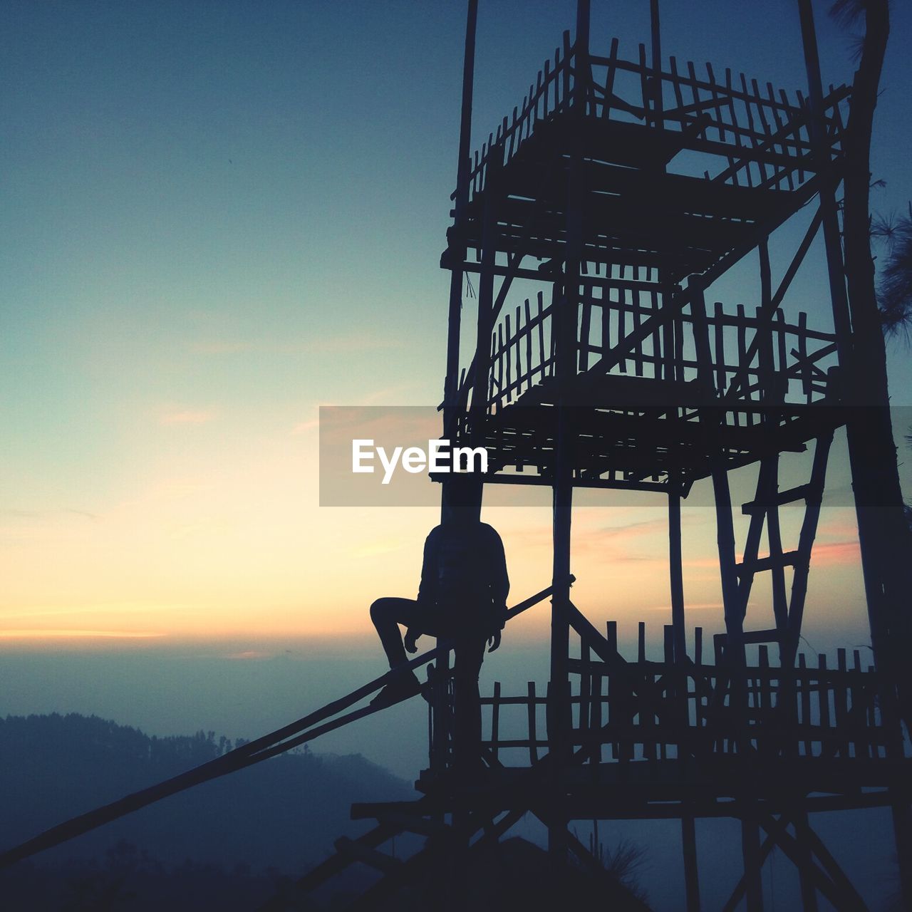 SILHOUETTE MAN STANDING BY RAILING AGAINST SEA DURING SUNSET