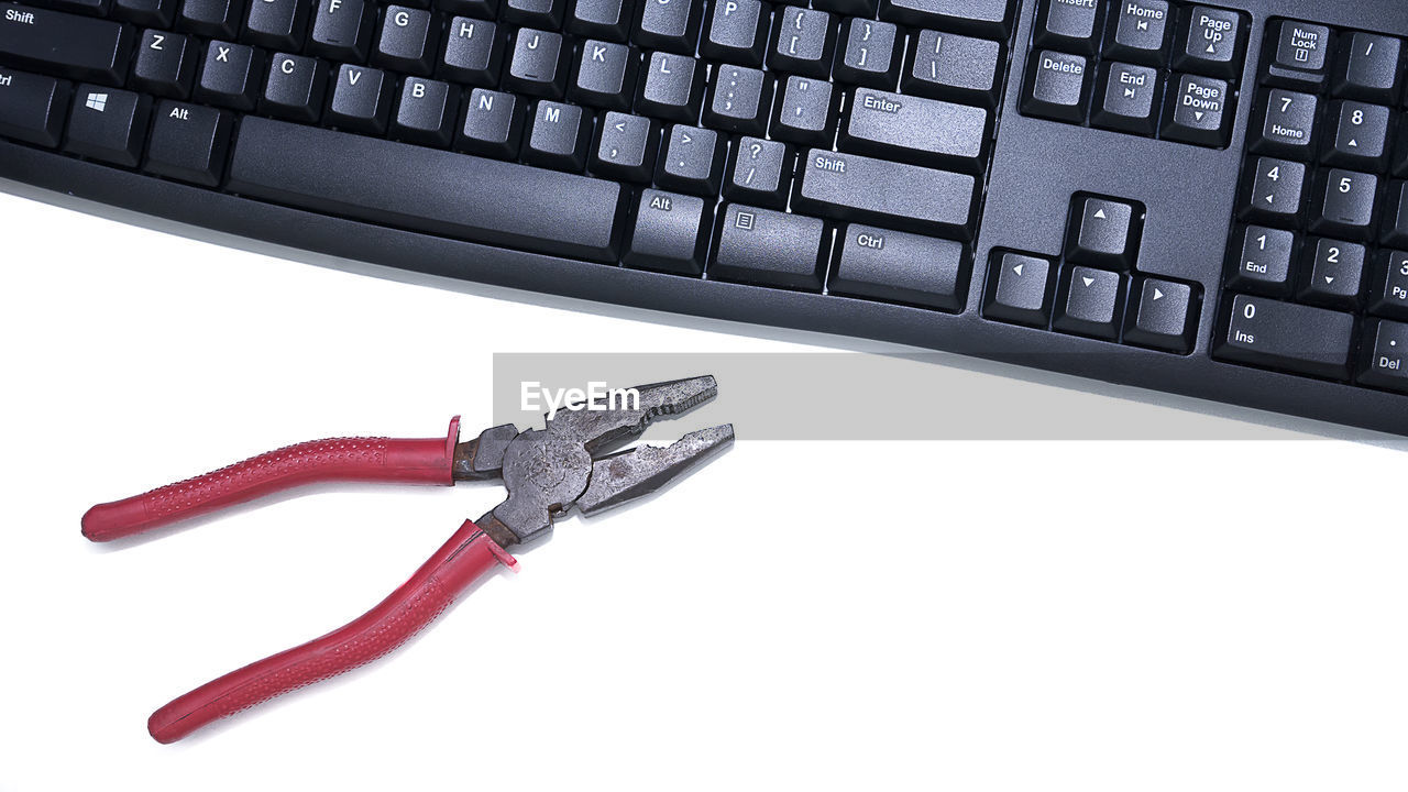 High angle view of computer keyboard and plier over white background