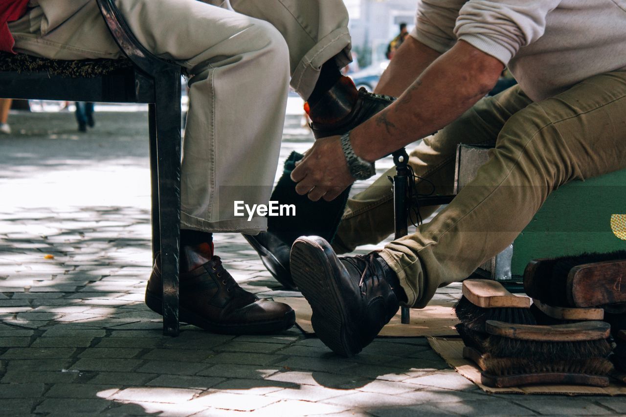 Low section of man polishing male customer shoe on footpath