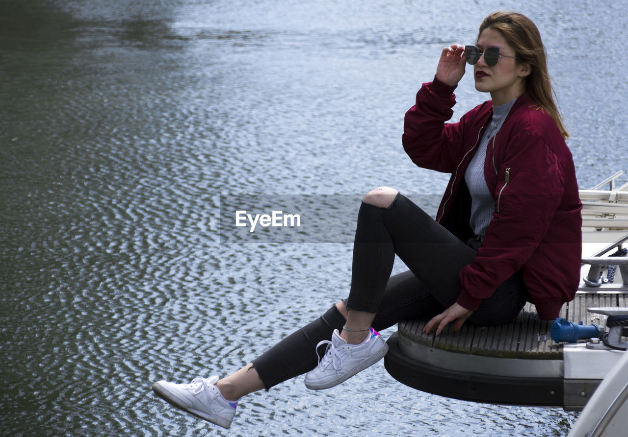 Full length of young woman sitting on pier over sea