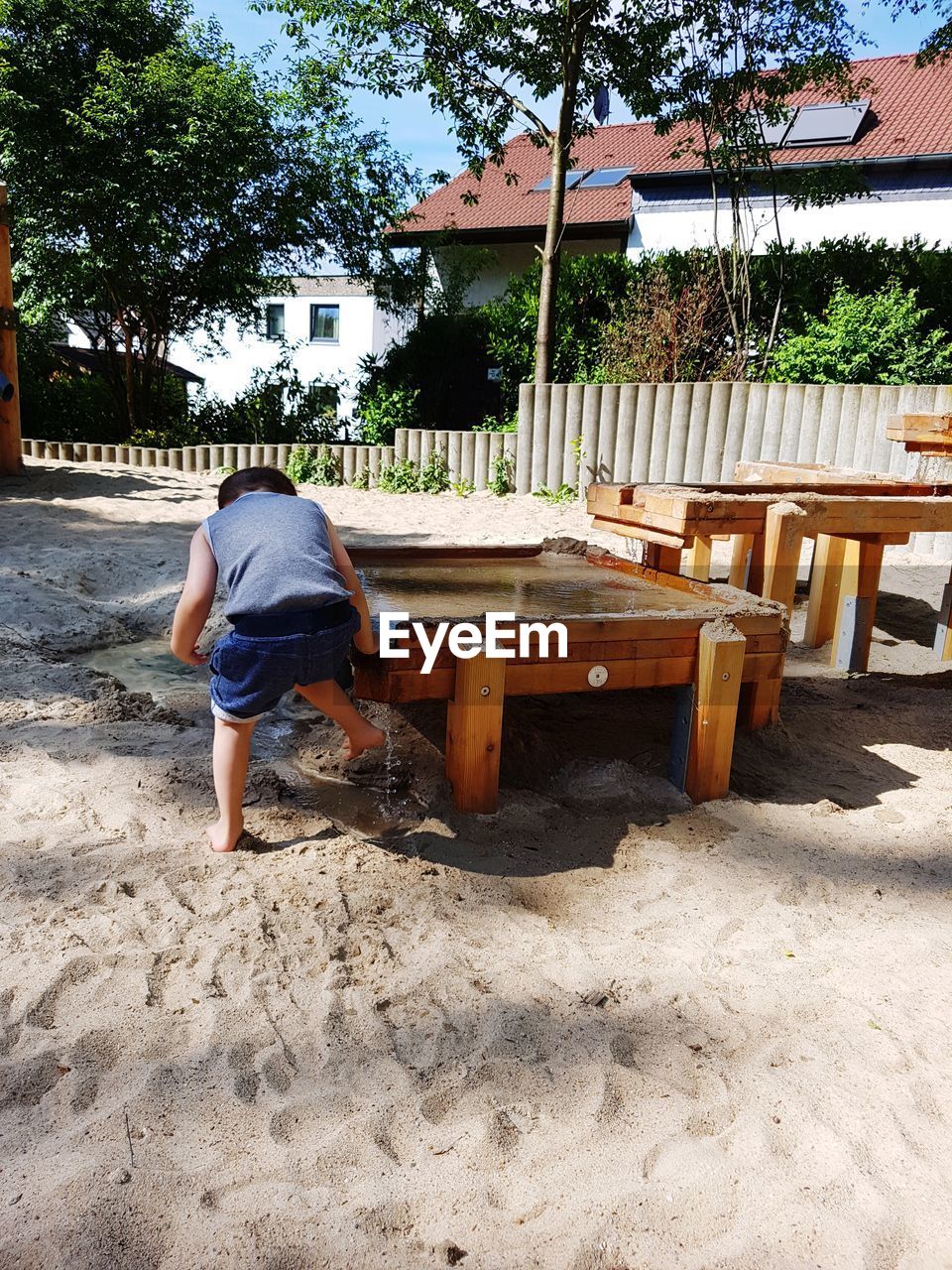 Rear view full length of boy playing with water by wooden built structure at sandy beach on sunny day