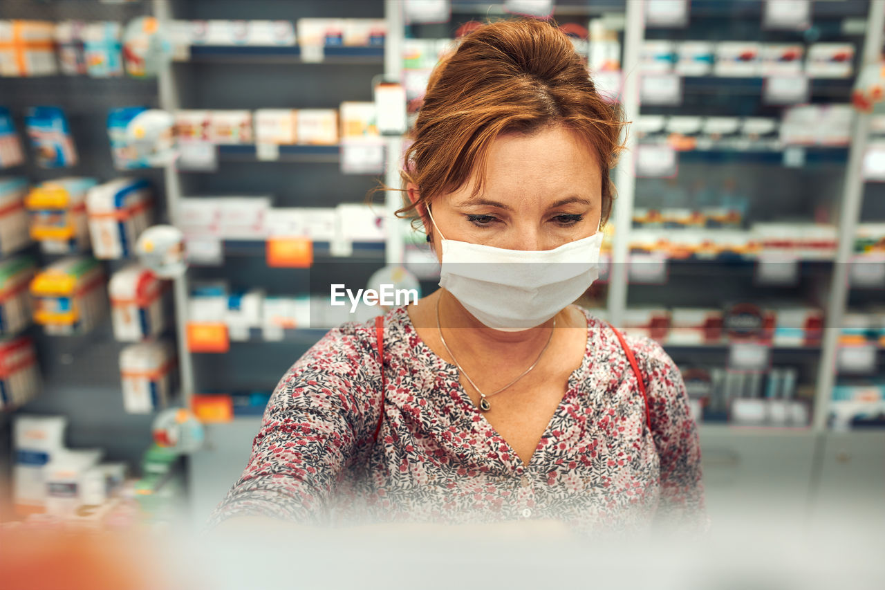 Woman shopping at pharmacy, buying medicines, wearing face mask to cover mouth and nose