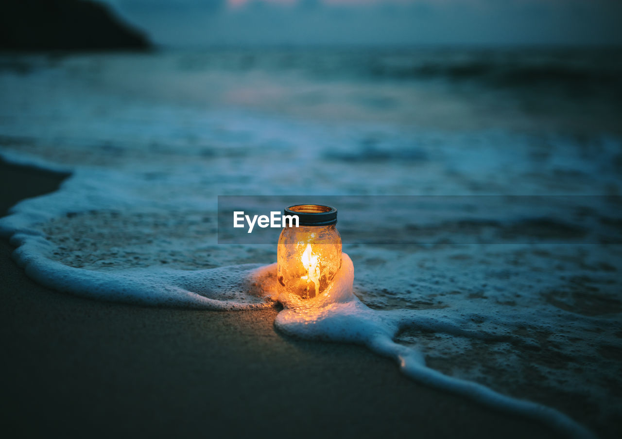 CLOSE-UP OF ILLUMINATED CANDLE ON BEACH