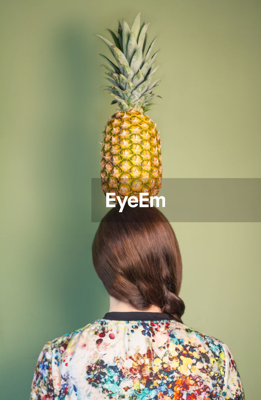 Close-up of woman holding pineapple against green background