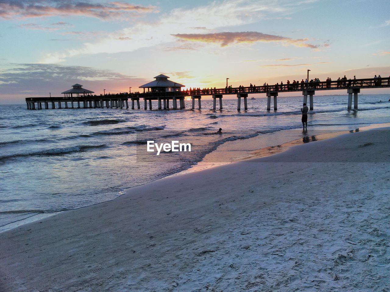 Pier on beach against sky during sunset