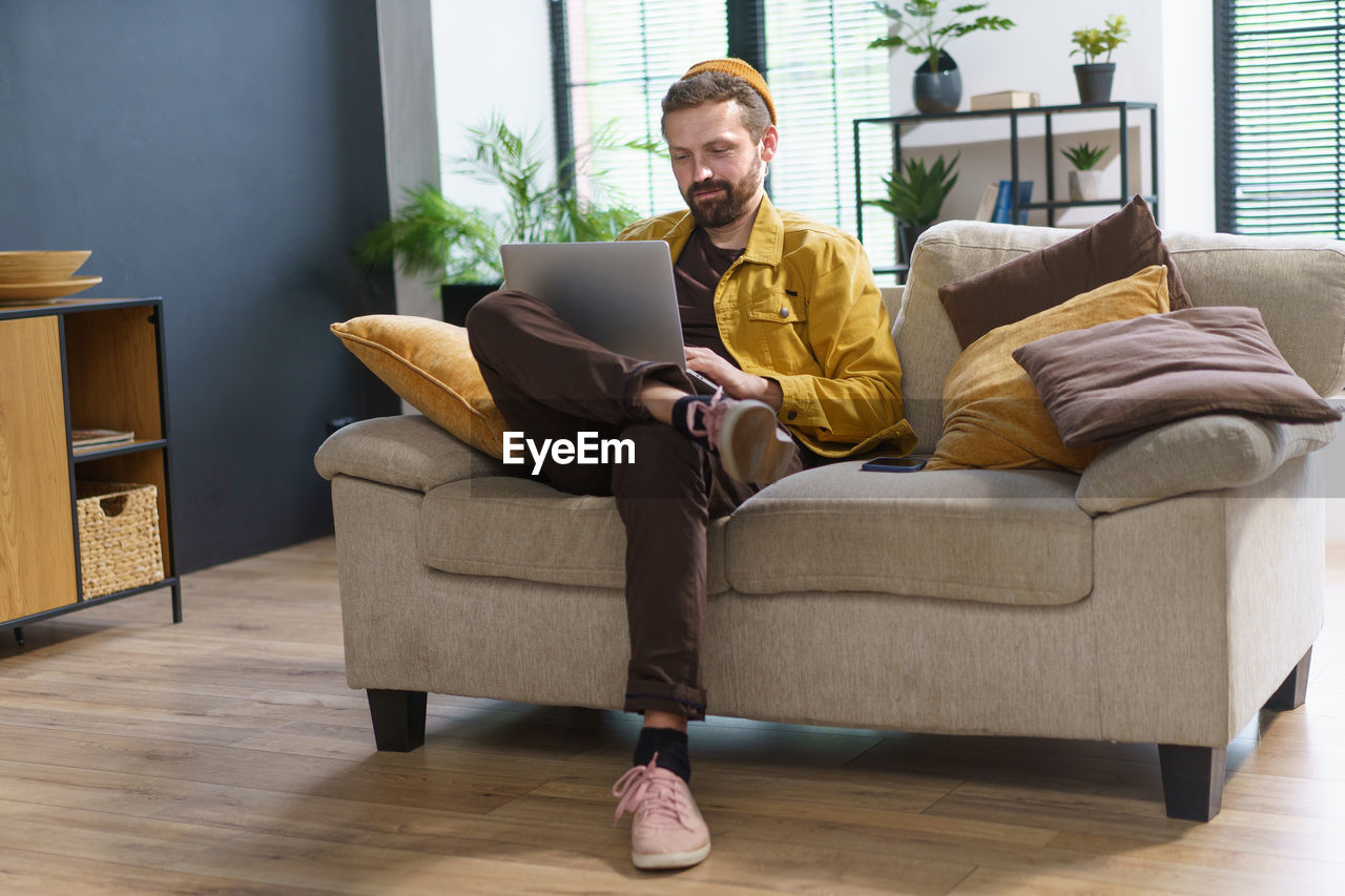 side view of woman using digital tablet while sitting on sofa at home