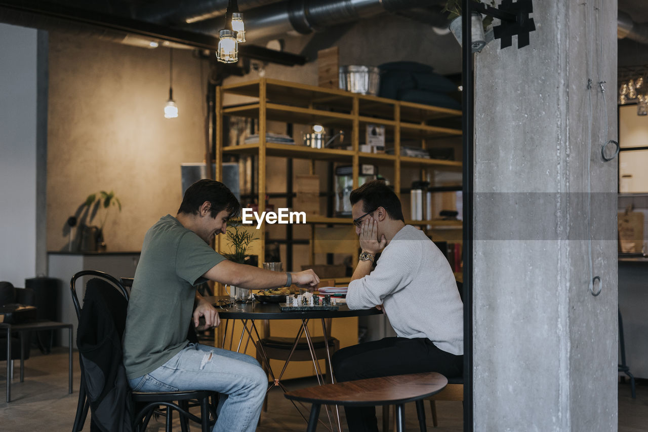 Male business colleagues playing chess on table at office cafeteria