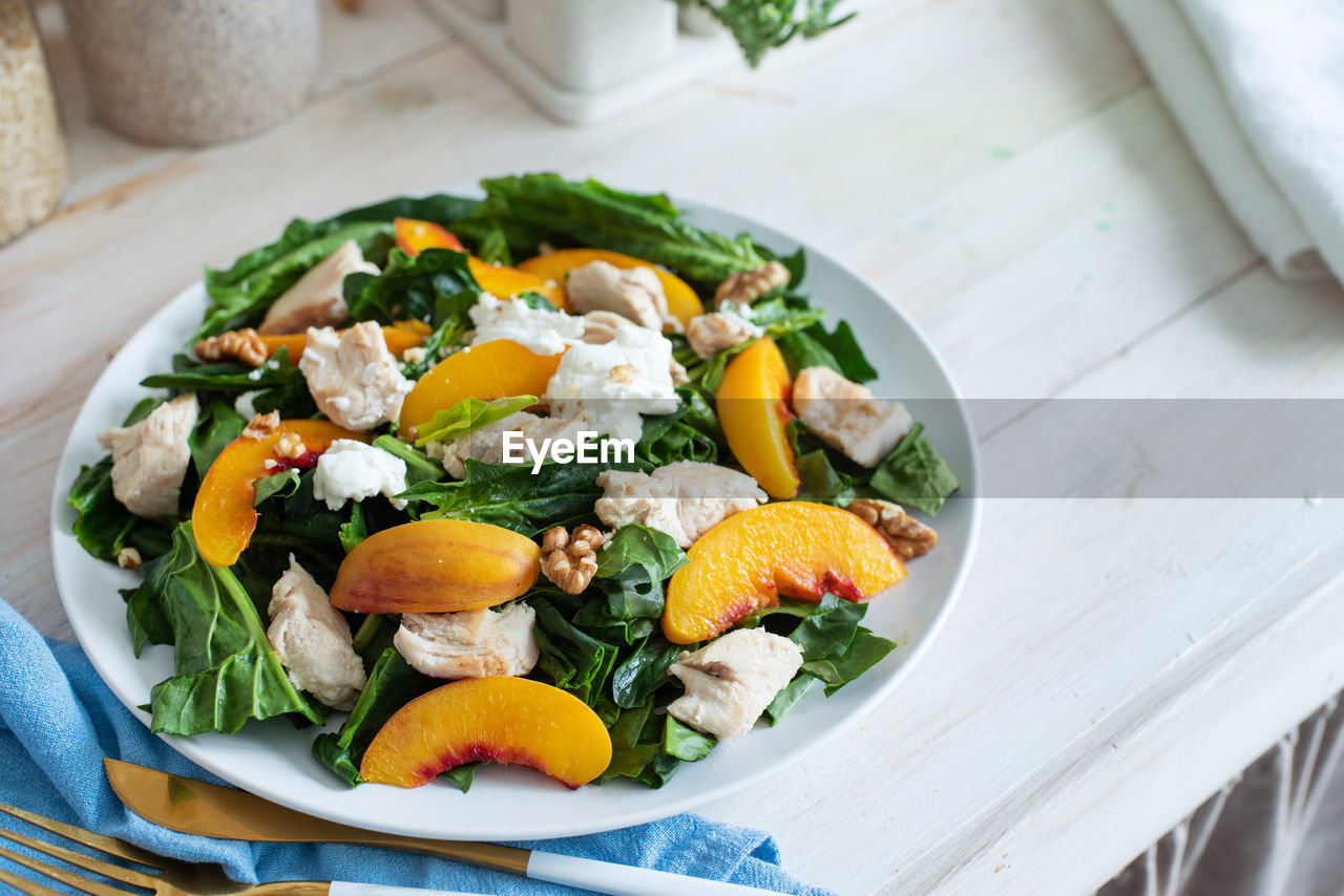 Top view plate with tasty peach and spinach salad on wooden table with copy space