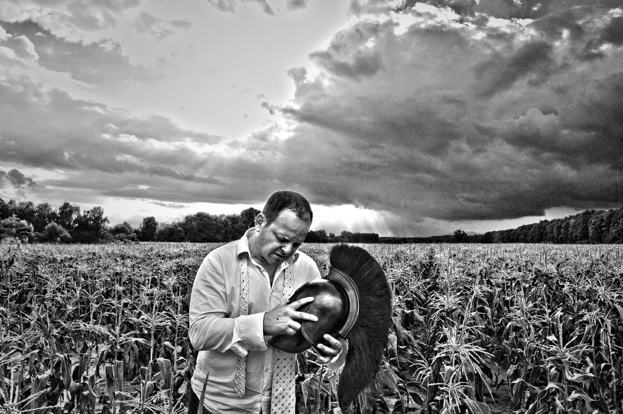 REAR VIEW OF MAN STANDING ON GRASSY FIELD AGAINST SKY