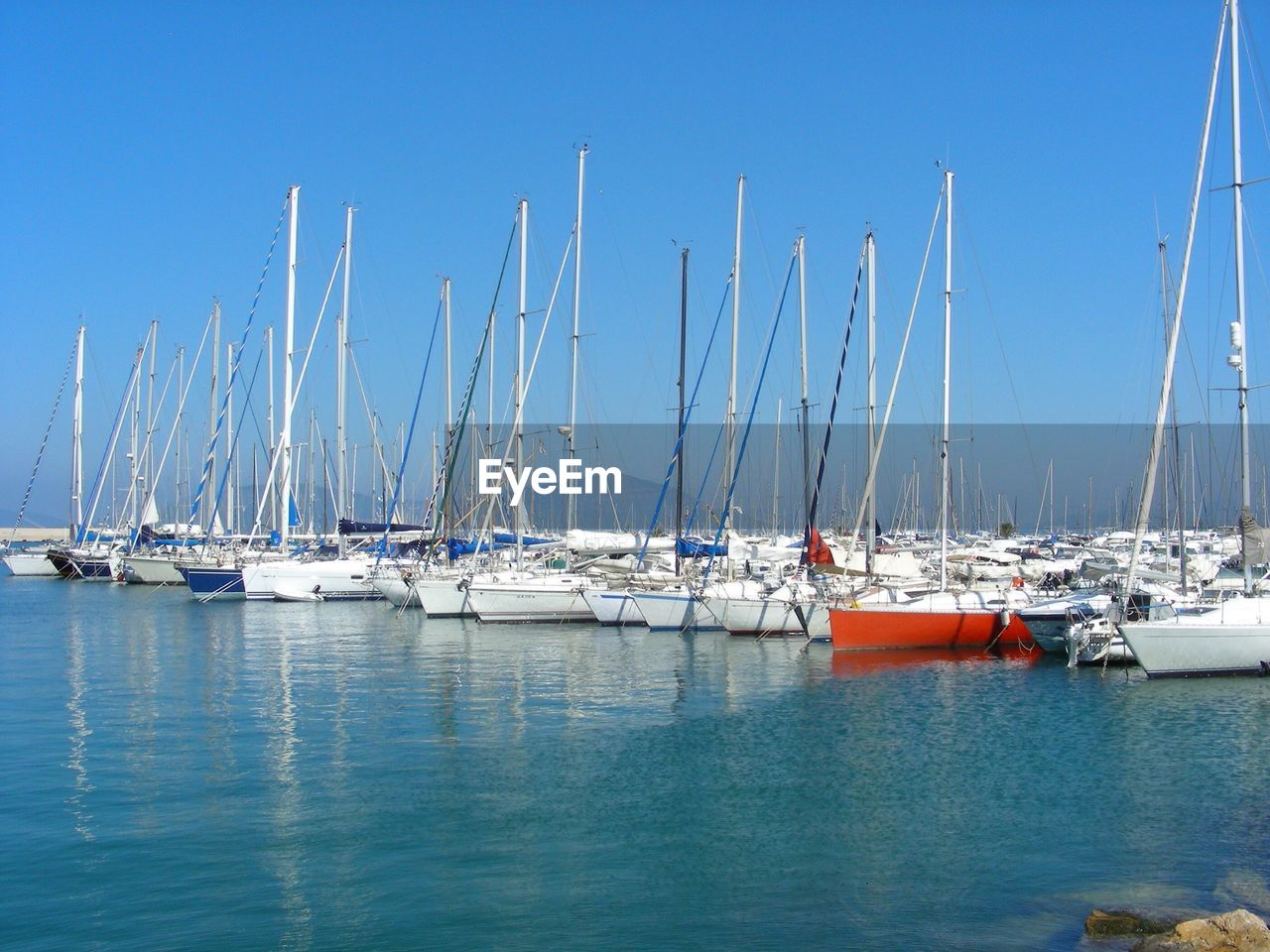 Boats moored in calm sea against clear blue sky