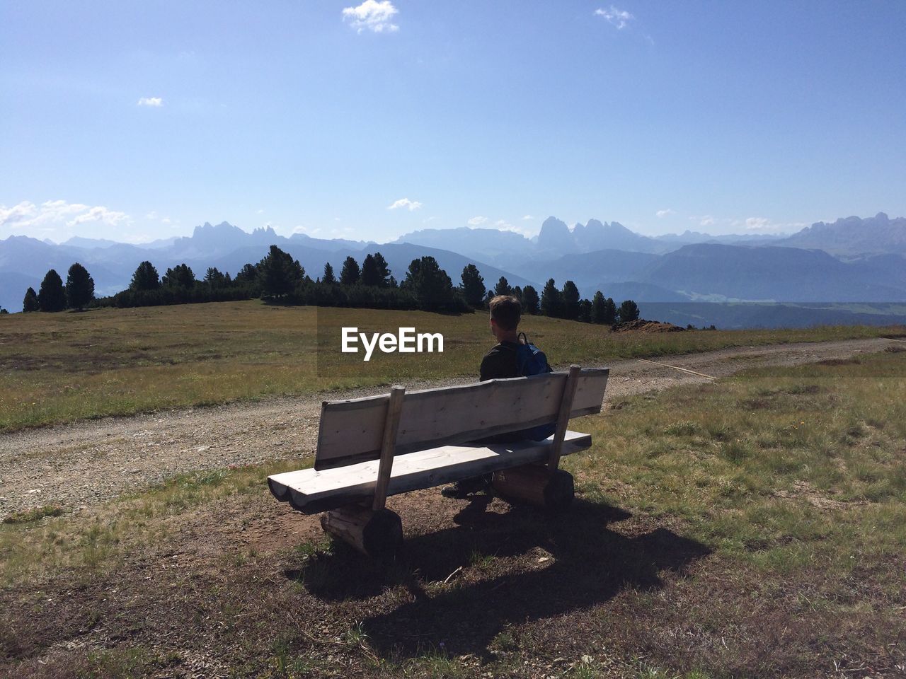 Rear view of hiker sitting on bench against sky