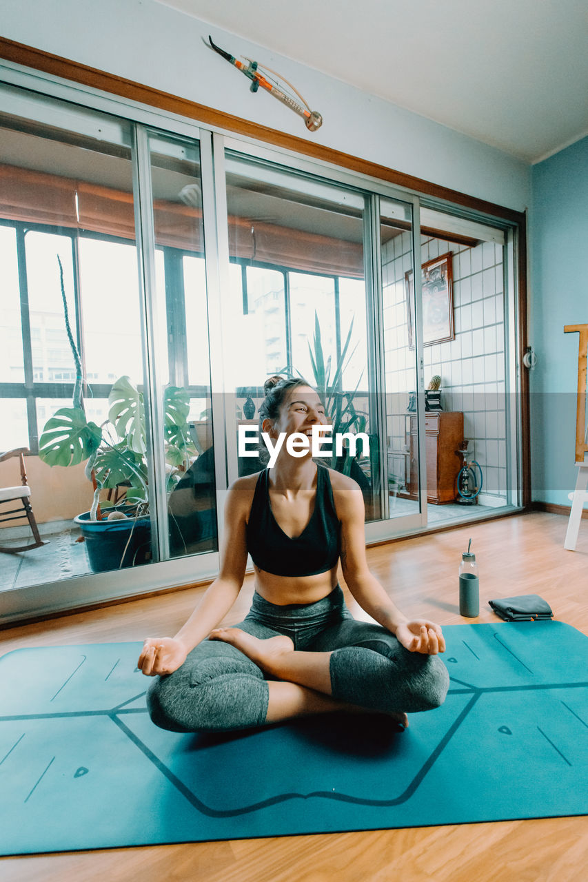 Happy young woman meditating on exercise mat at home