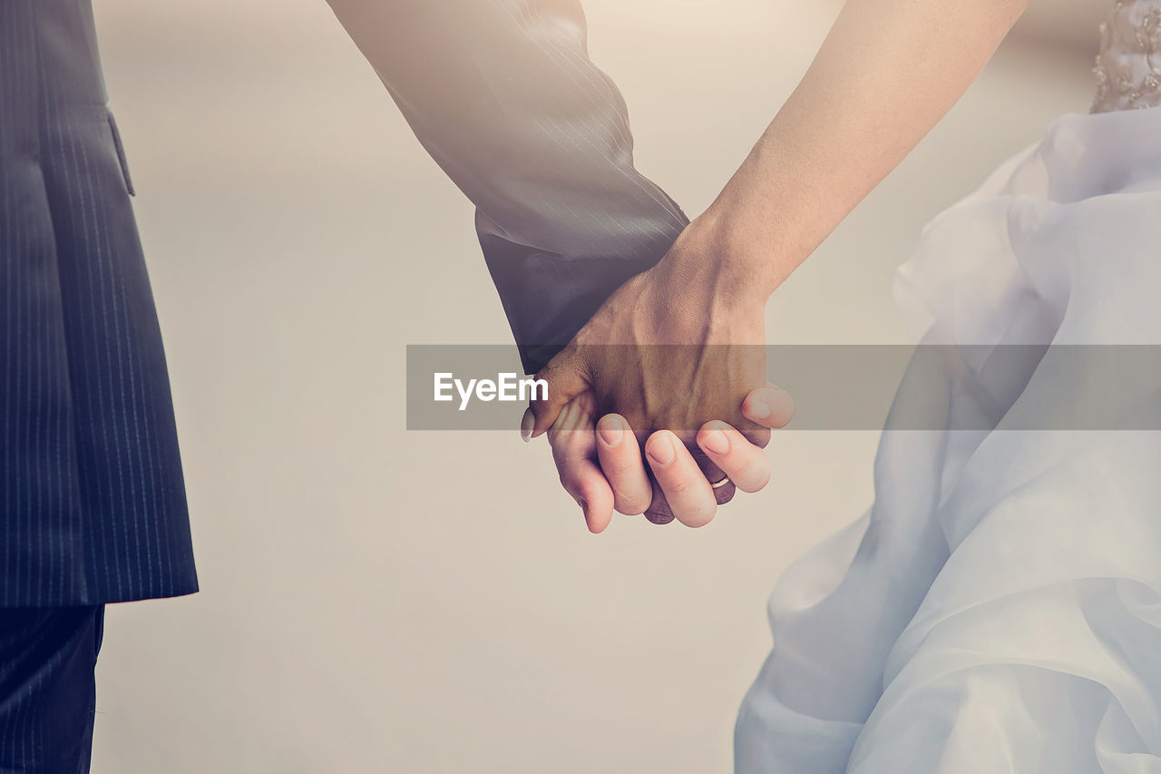 Midsection of wedding couple holding hands outdoors