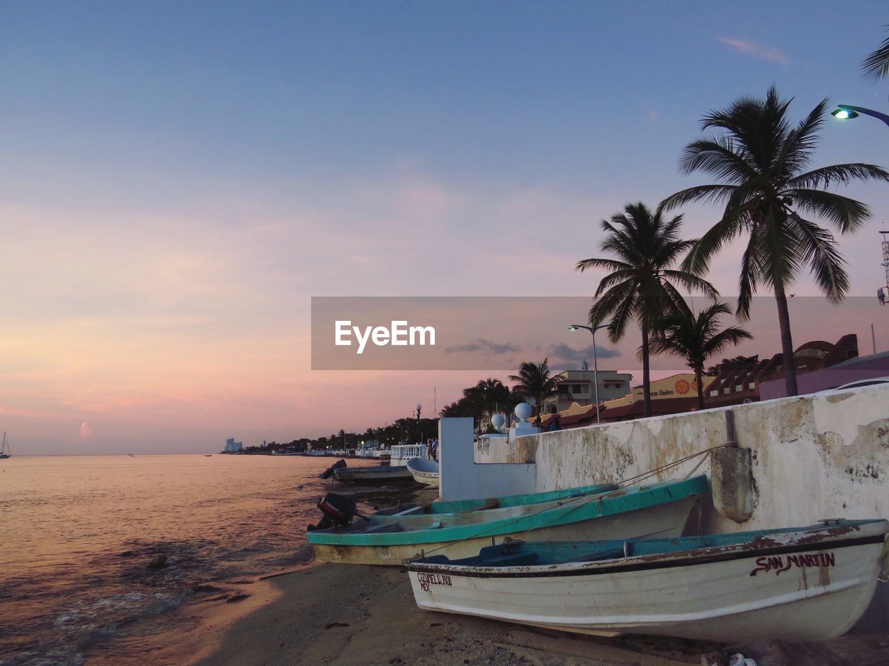 Boats moored at beach against sky at dusk