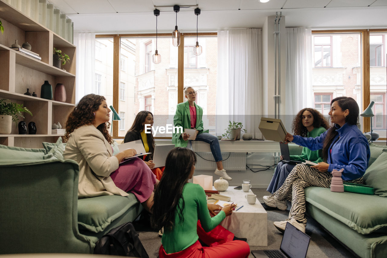 Female colleagues holding box while discussing with business coworkers during meeting at office