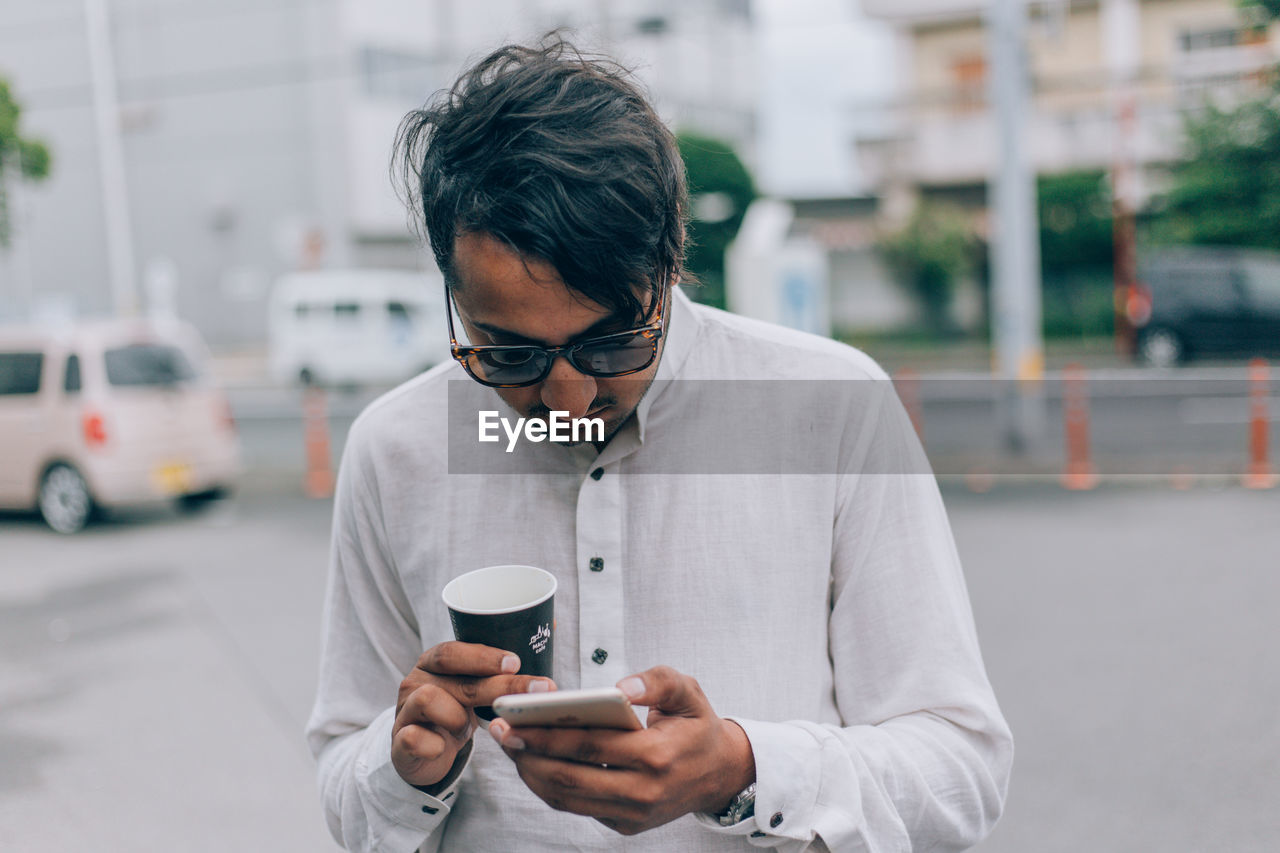 YOUNG MAN USING PHONE WHILE STANDING ON STREET