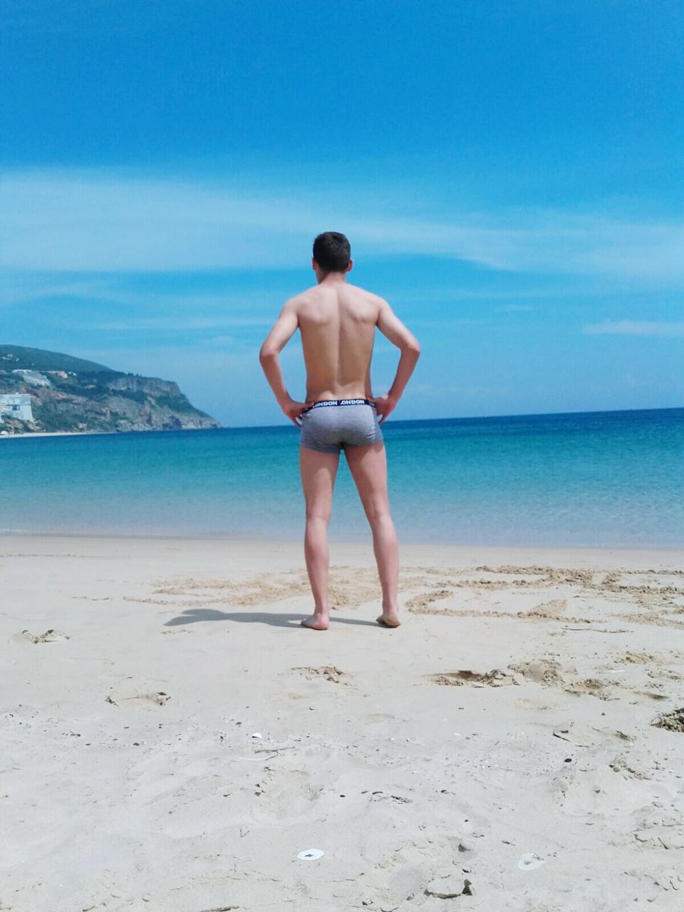 REAR VIEW OF MAN STANDING ON BEACH