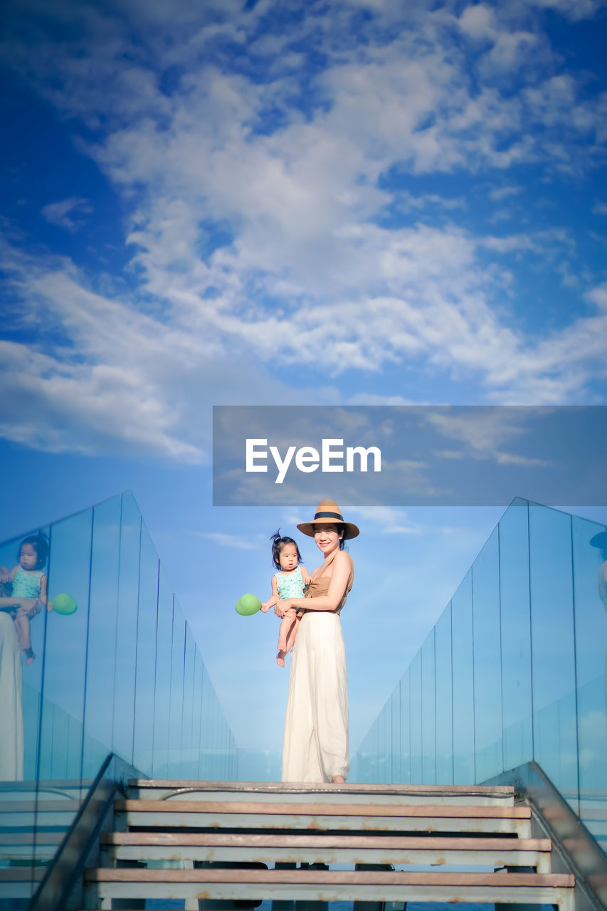 Portrait of woman standing with daughter against sky