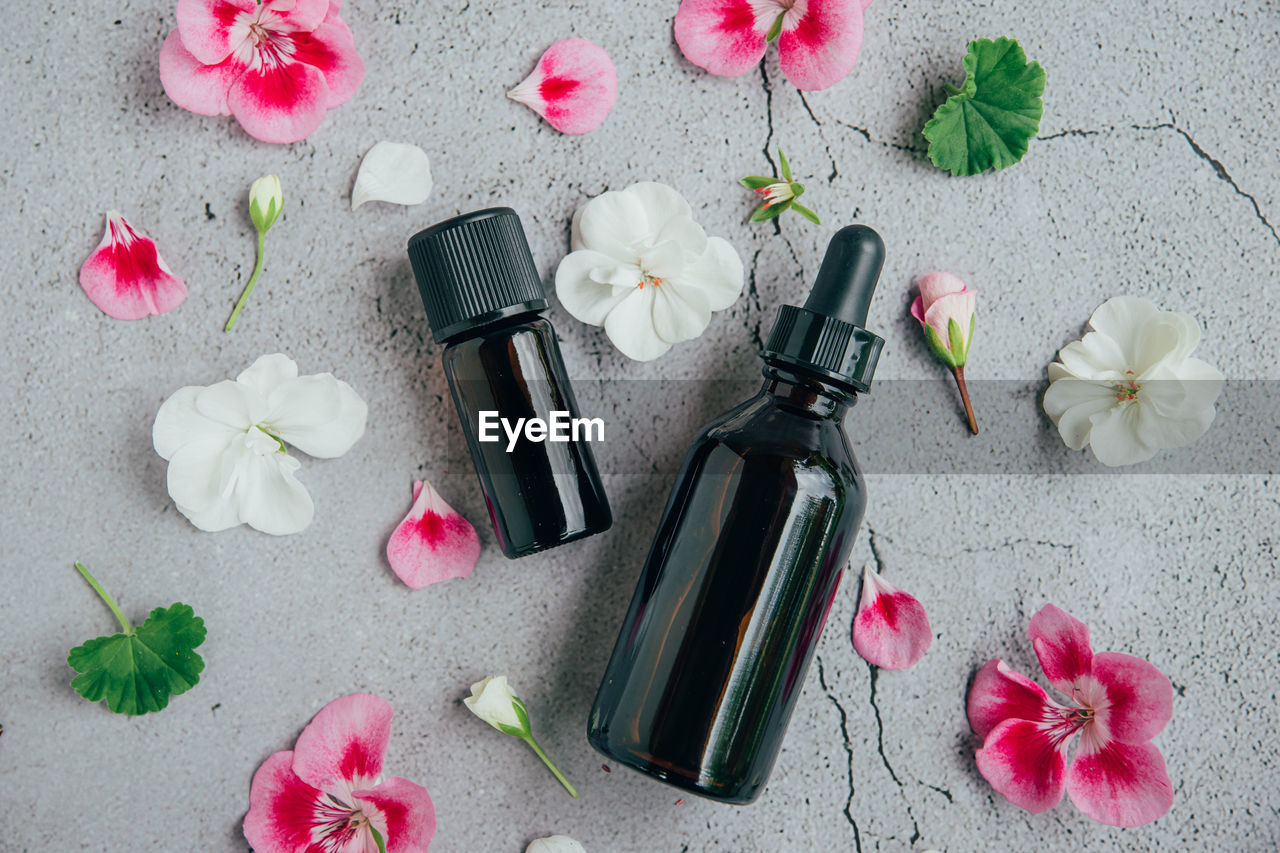 Top view of glass bottles of geranium essential oil with fresh pink and white flowers and petals 