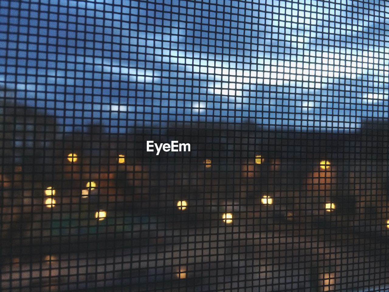 Illuminated city seen through metal grate