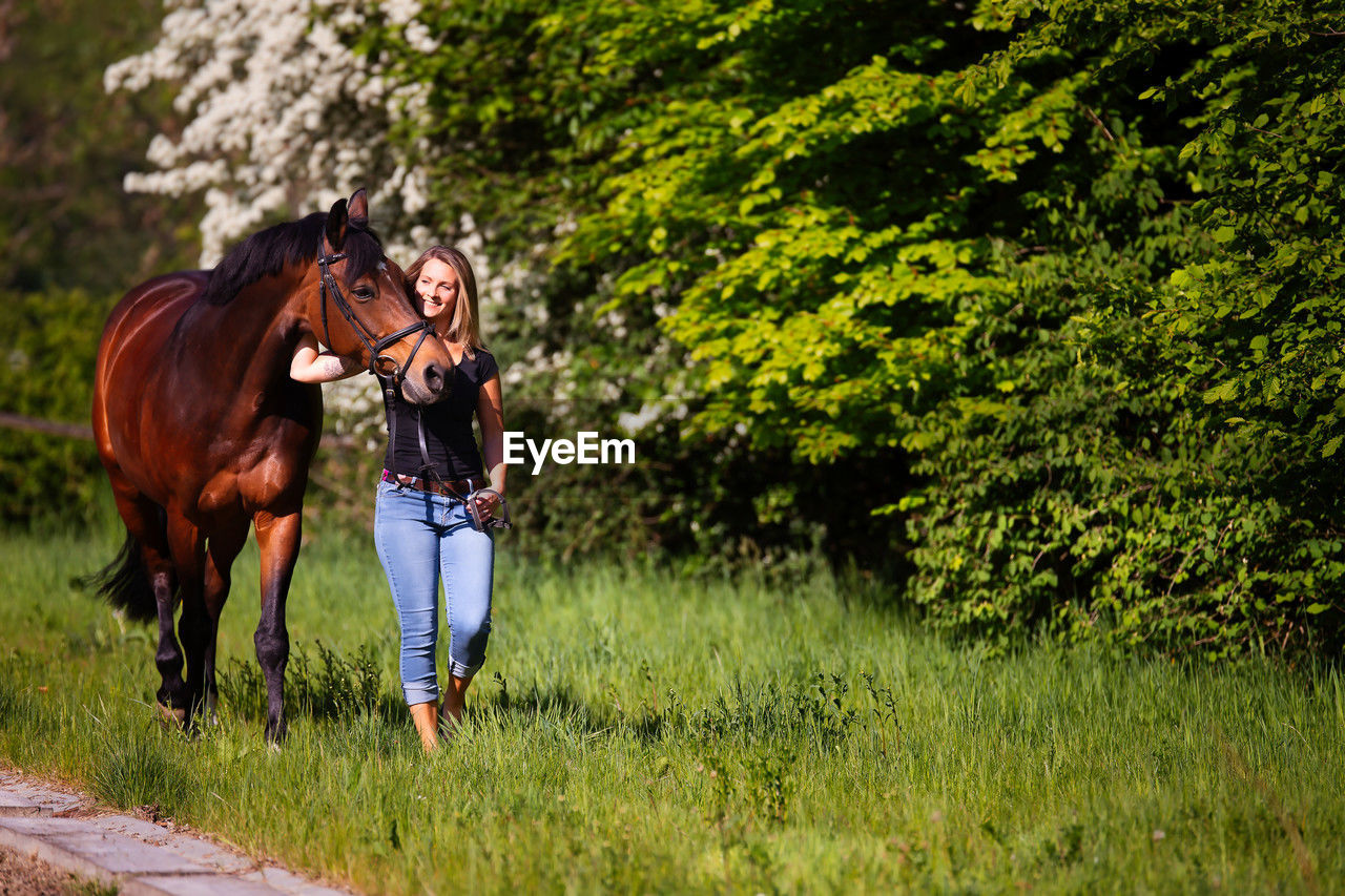 horse, mammal, domestic animals, animal, animal themes, plant, pet, livestock, meadow, animal wildlife, one animal, grass, nature, tree, rural area, green, adult, land, field, pasture, women, activity, leisure activity, full length, lifestyles, day, young adult, one person, outdoors, casual clothing, landscape, growth, emotion, rural scene, brown, female, beauty in nature, sunlight, horseback riding, riding, positive emotion, plain, environment, love, hairstyle, happiness, equestrian sport, child, agriculture, standing, herbivorous